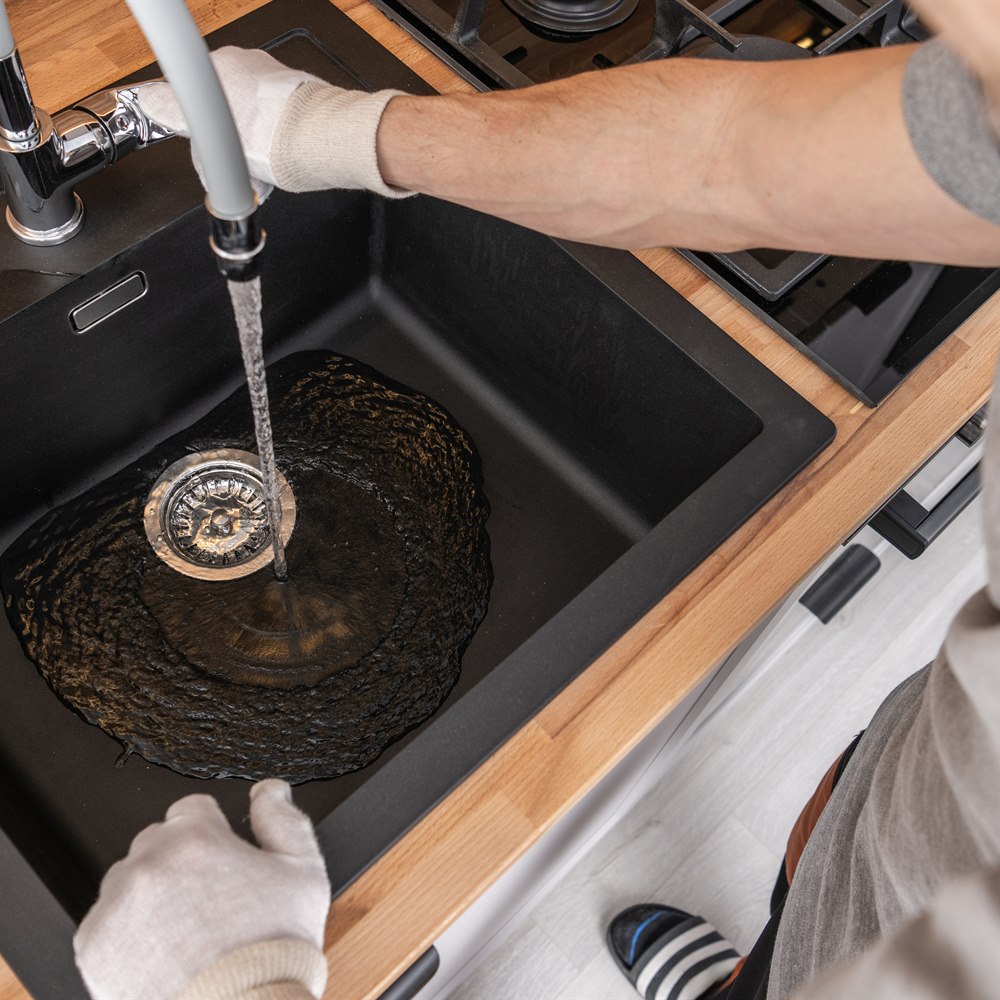 Adult cleaning a black kitchen sink with water