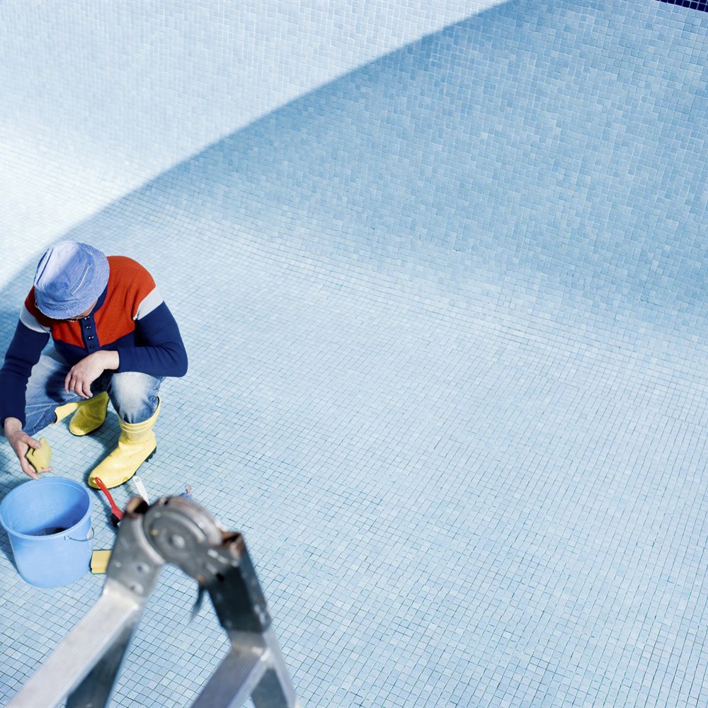 Adult cleaning an empty tiled swimming pool