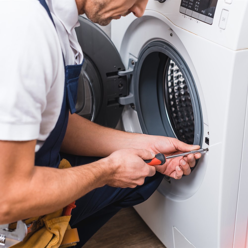 Appliance repairman fixing washing machine in home