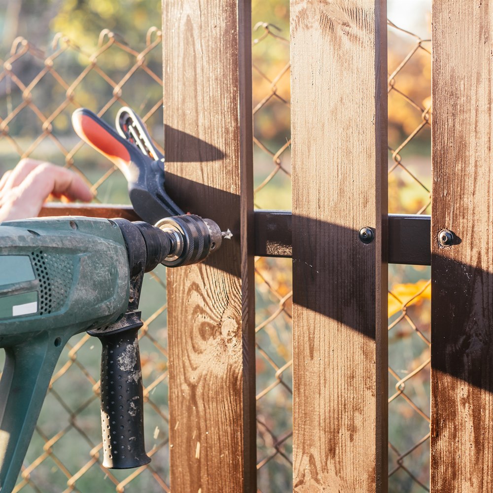 Building fence with electric drill on sunny day