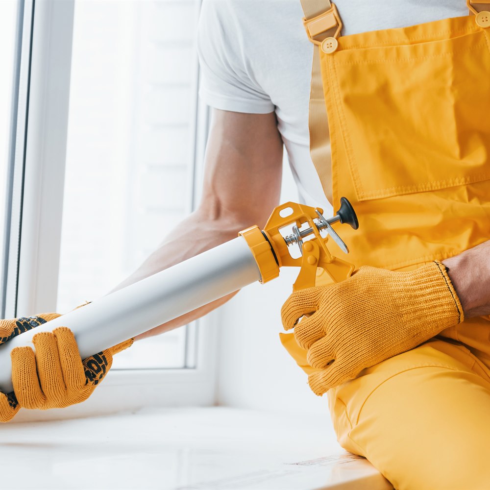 Construction worker seals window frame with caulk