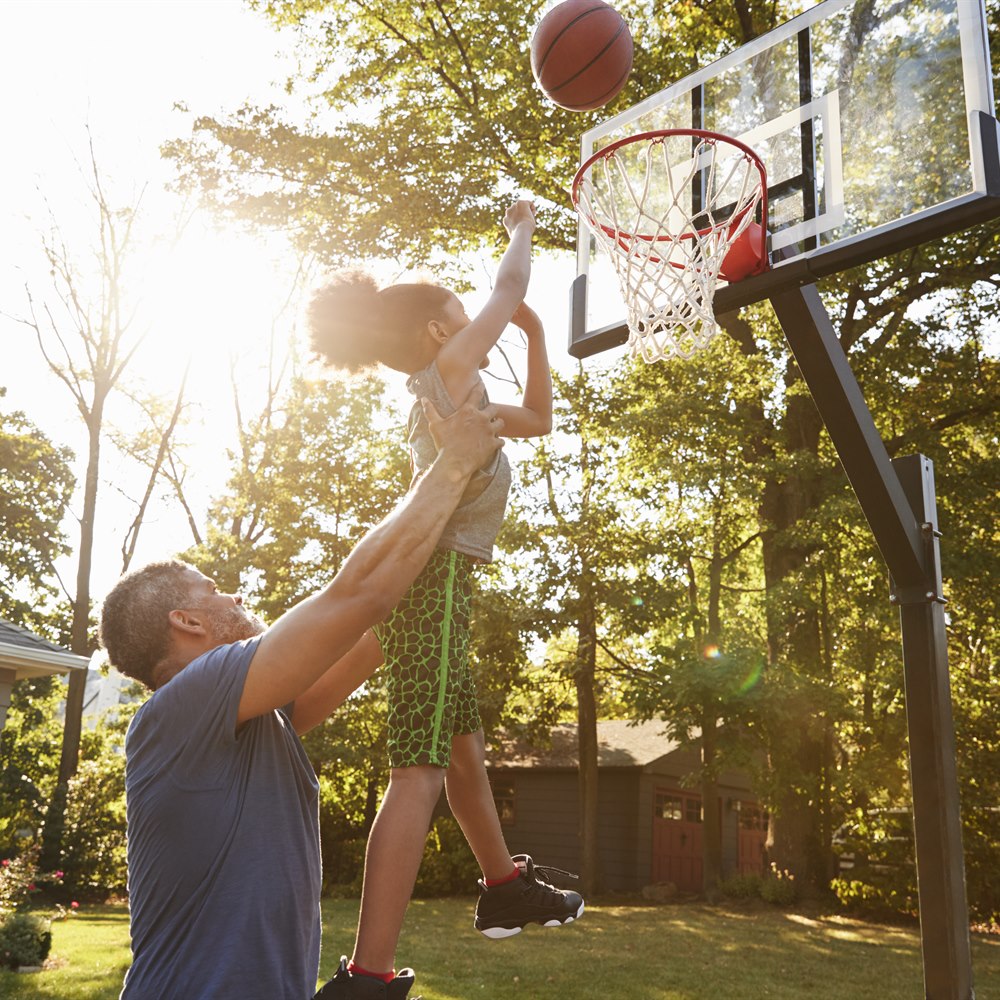 Dad lifts child to reach basketball net outside