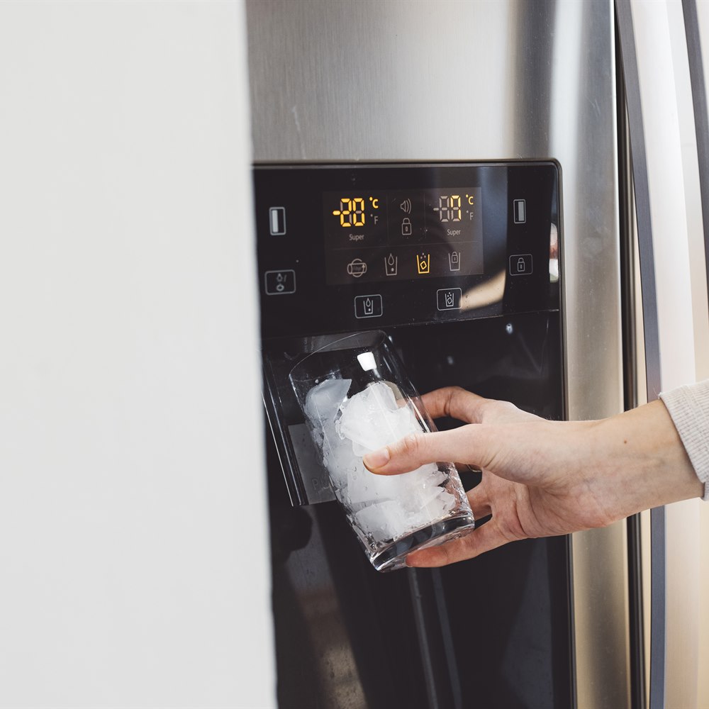 Hand holding glass filled with ice from refrigerator