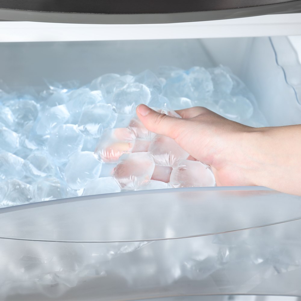 Hand reaching into freezer for ice in bag
