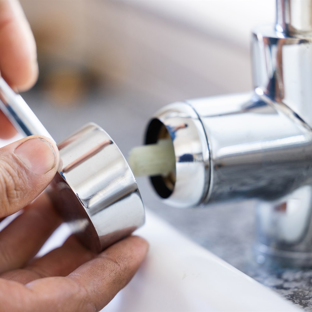 Hands repairing a faucet with a tool