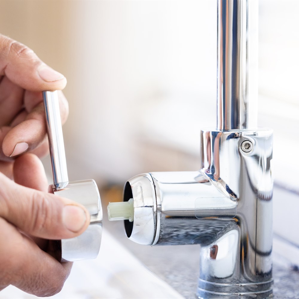 Hands repairing a shiny chrome water faucet
