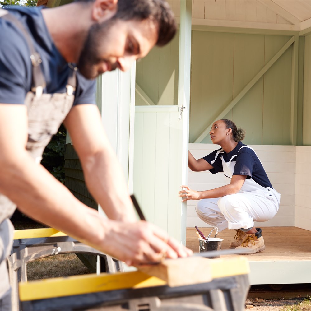 Man and woman painting small shed