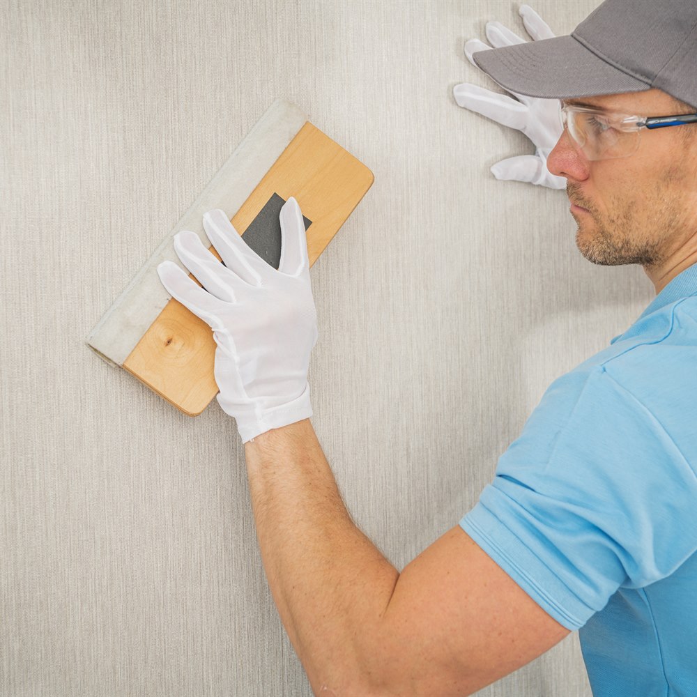 man-applies-wallpaper-to-a-wall-indoors Man applies wallpaper to a wall indoors