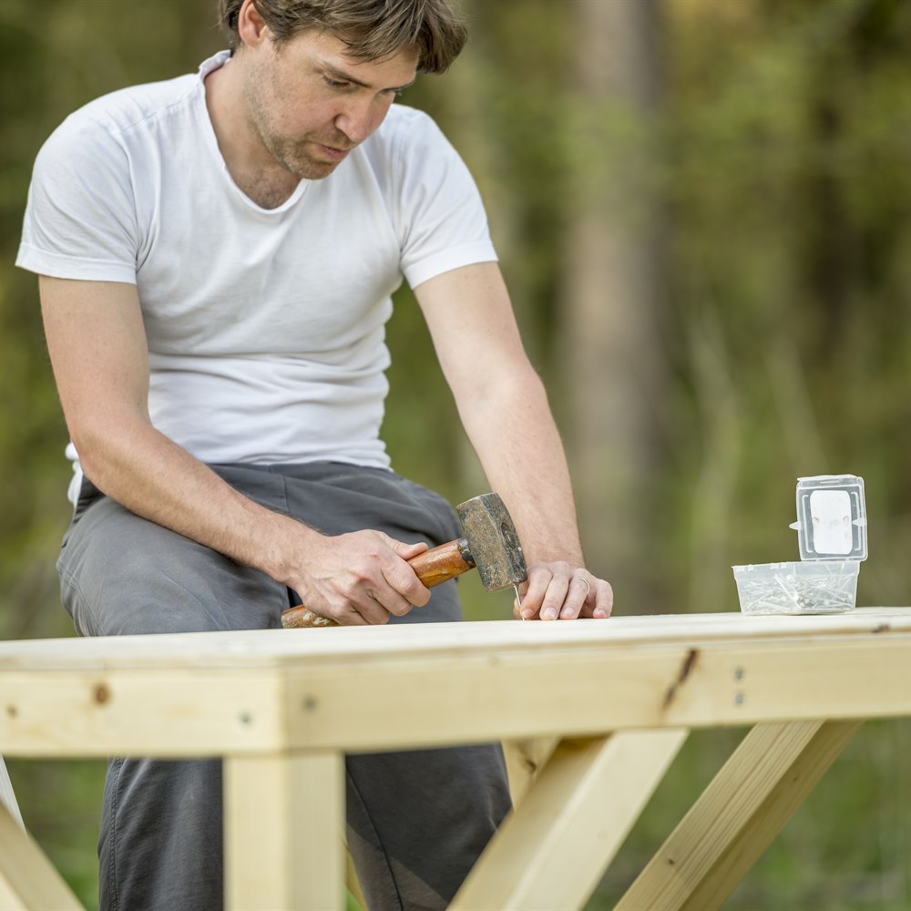 man-hammering-nail-into-wood-outside-building-proj Man hammering nail into wood outside building project
