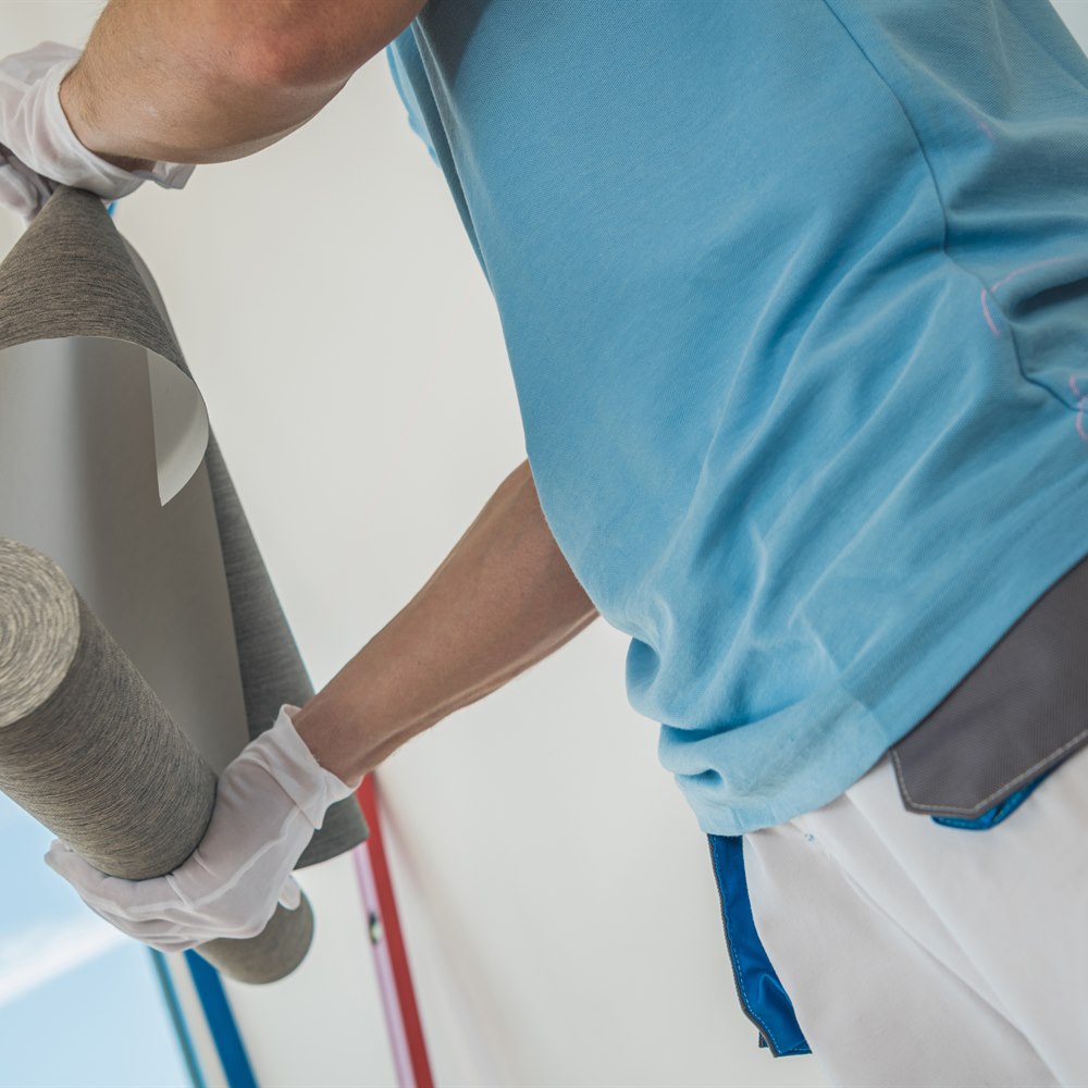 Man holding a roll of grey textured wallpaper