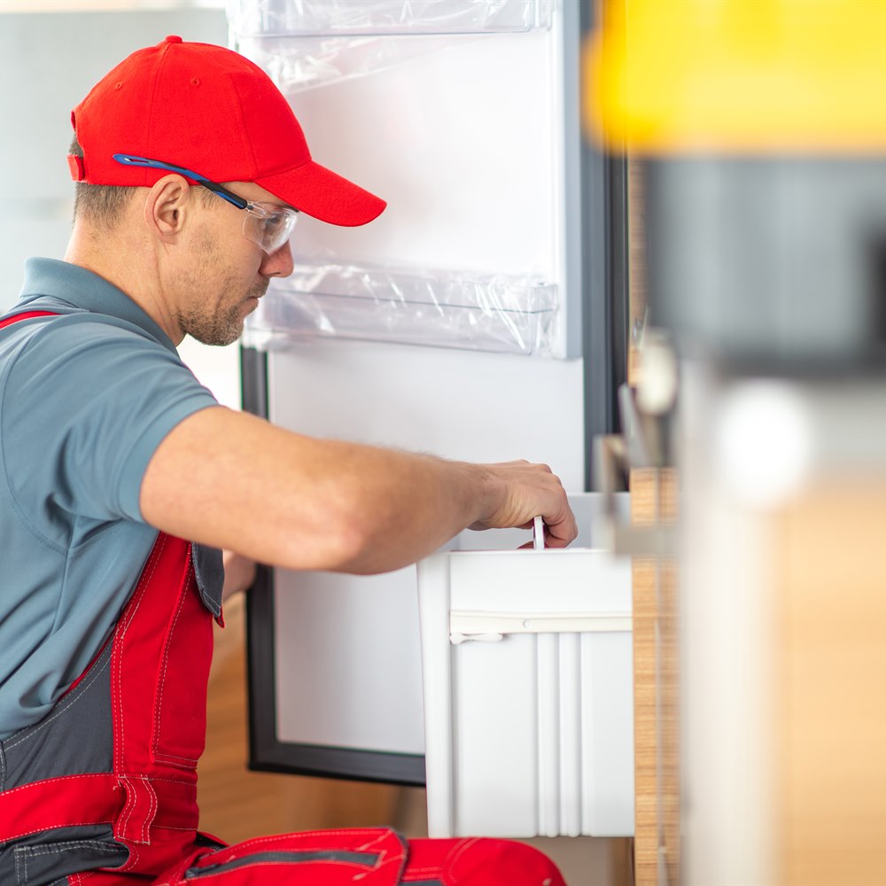 Man repairing appliance indoors wearing red overalls