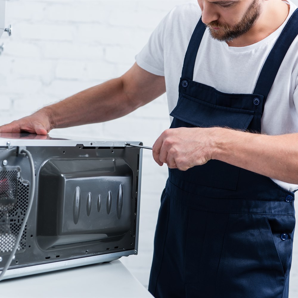 Man repairing microwave with screwdriver in kitchen