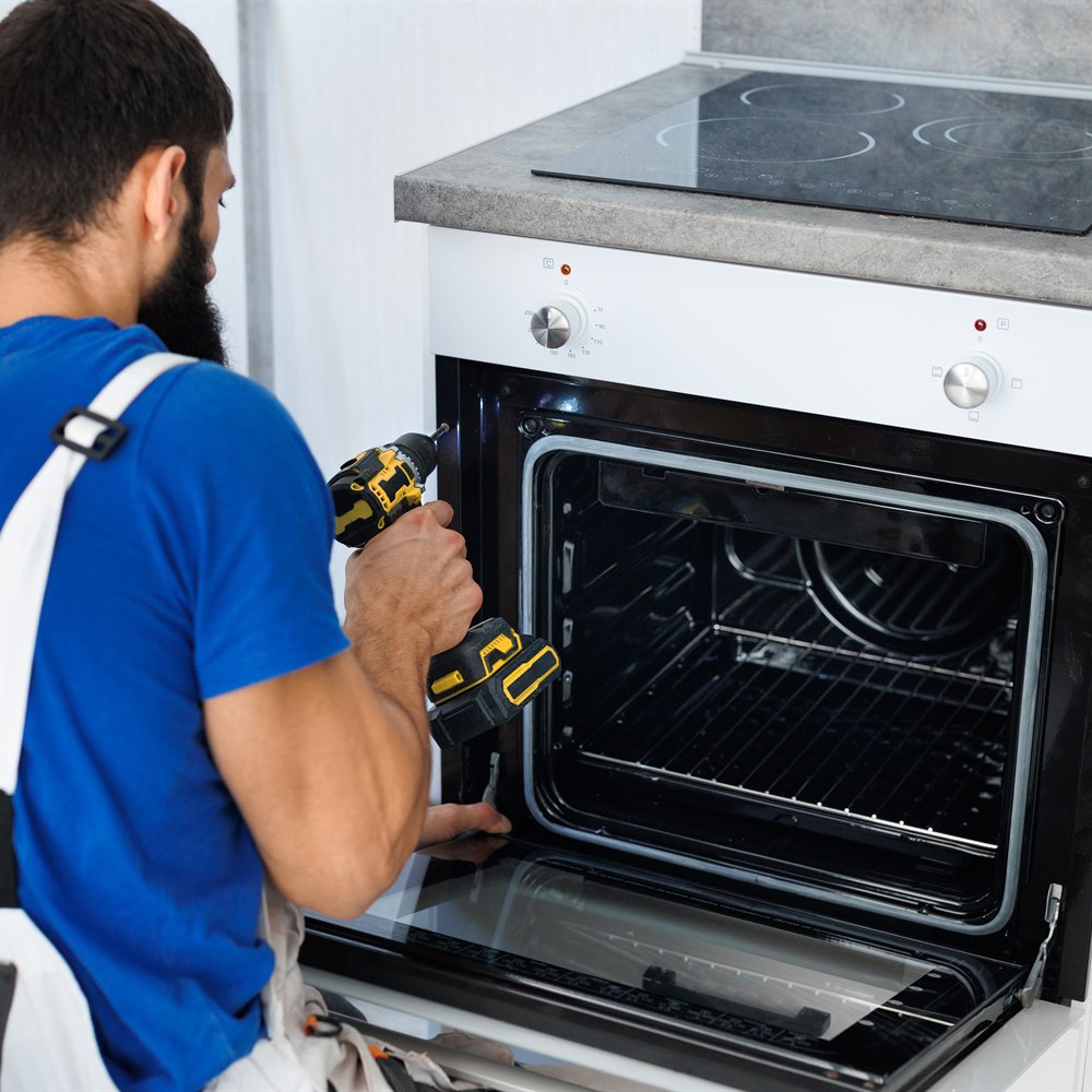Man repairing oven with power drill in kitchen