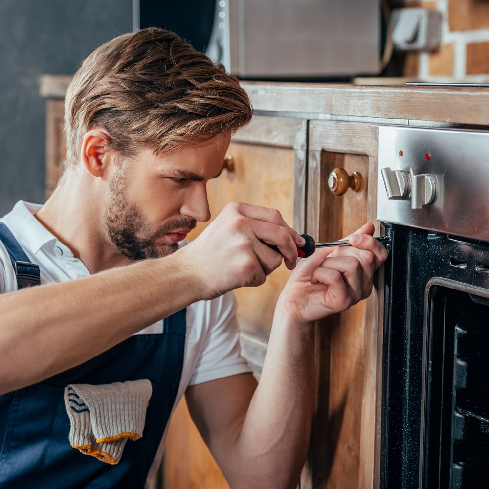 Man repairing oven with screwdriver in kitchen