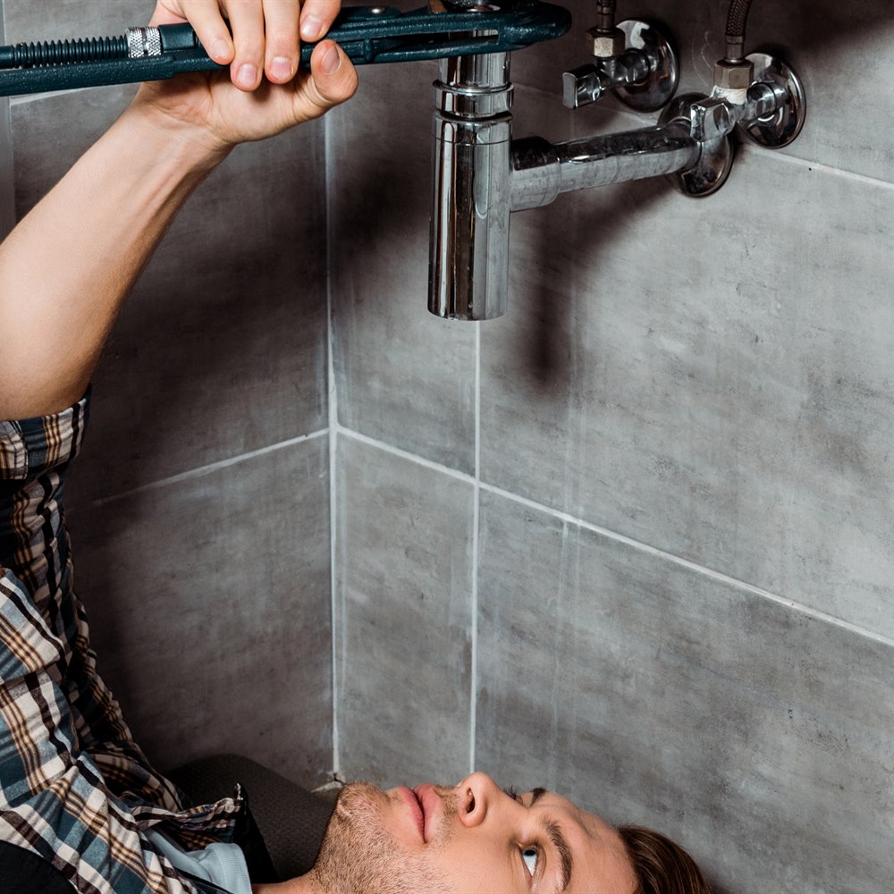 Man repairing sink pipe lying on bathroom floor