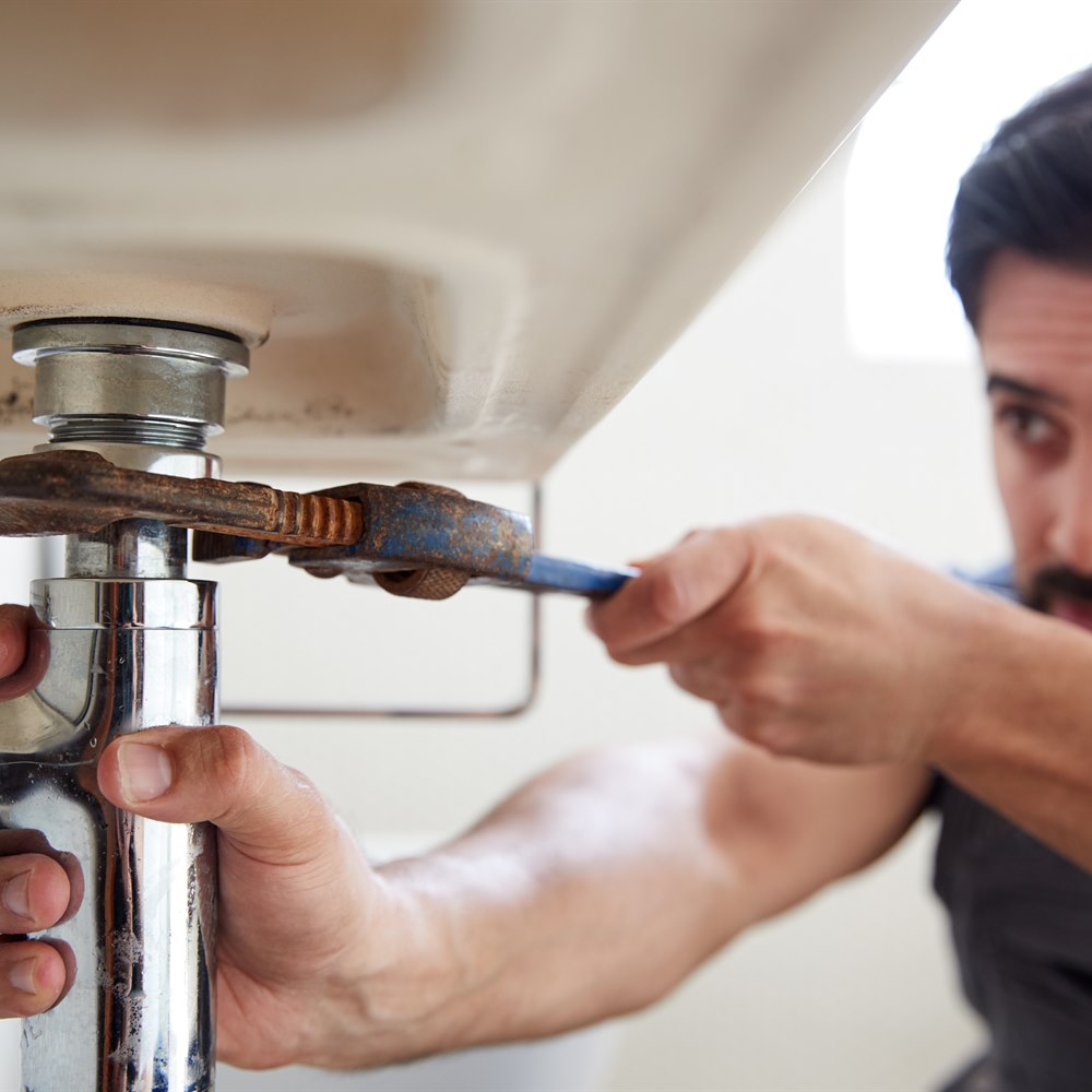 Man repairing sink with pipe wrench indoors