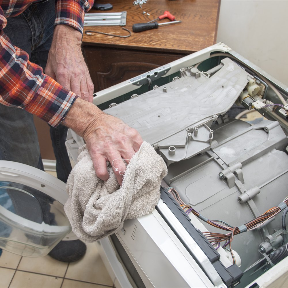Man repairing washing machine with cloth in home