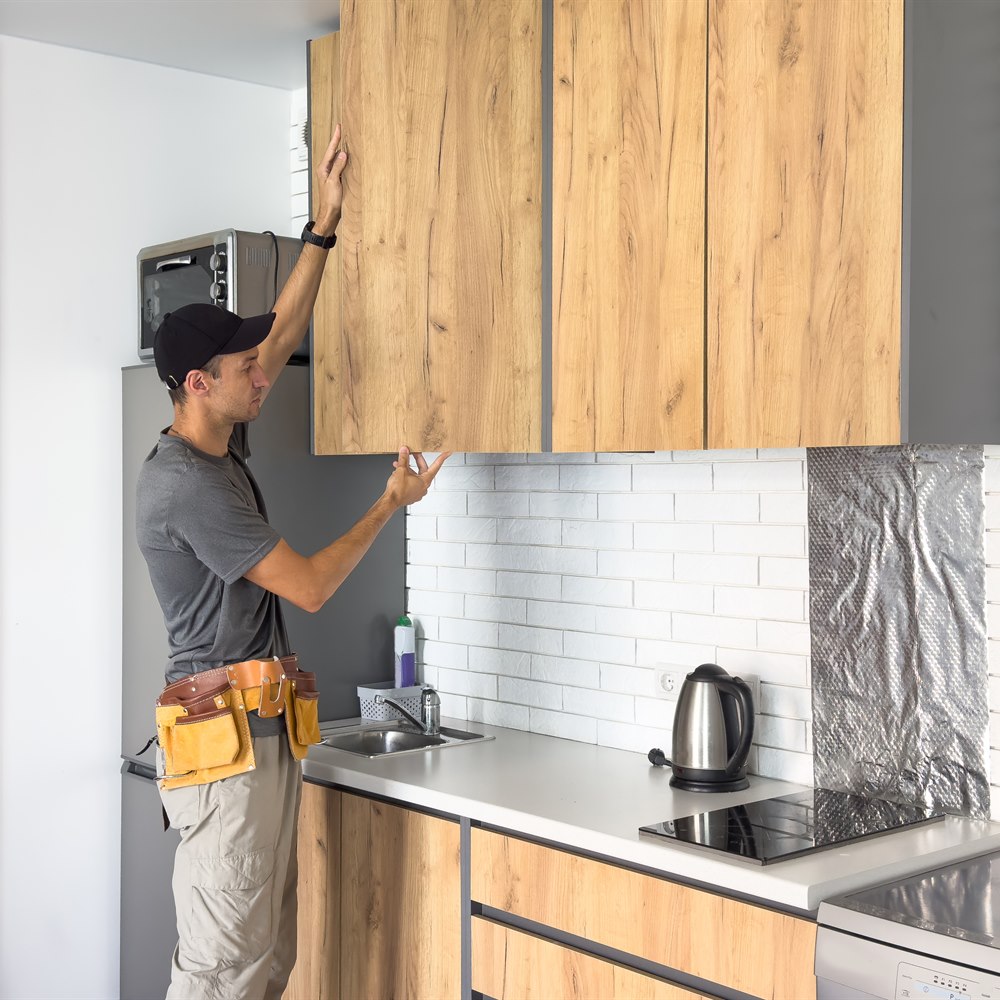 Man repairing wooden cabinets in a kitchen