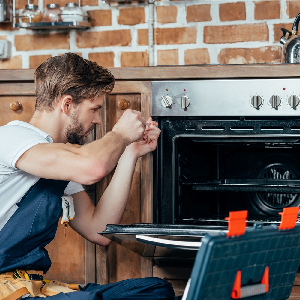 Man repairs an oven in a kitchen