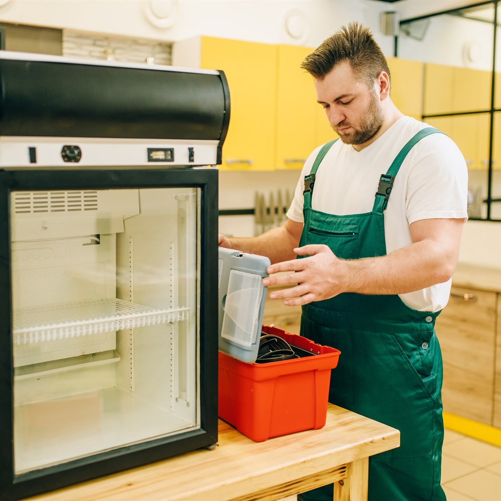 Man repairs refrigerator in bright kitchen