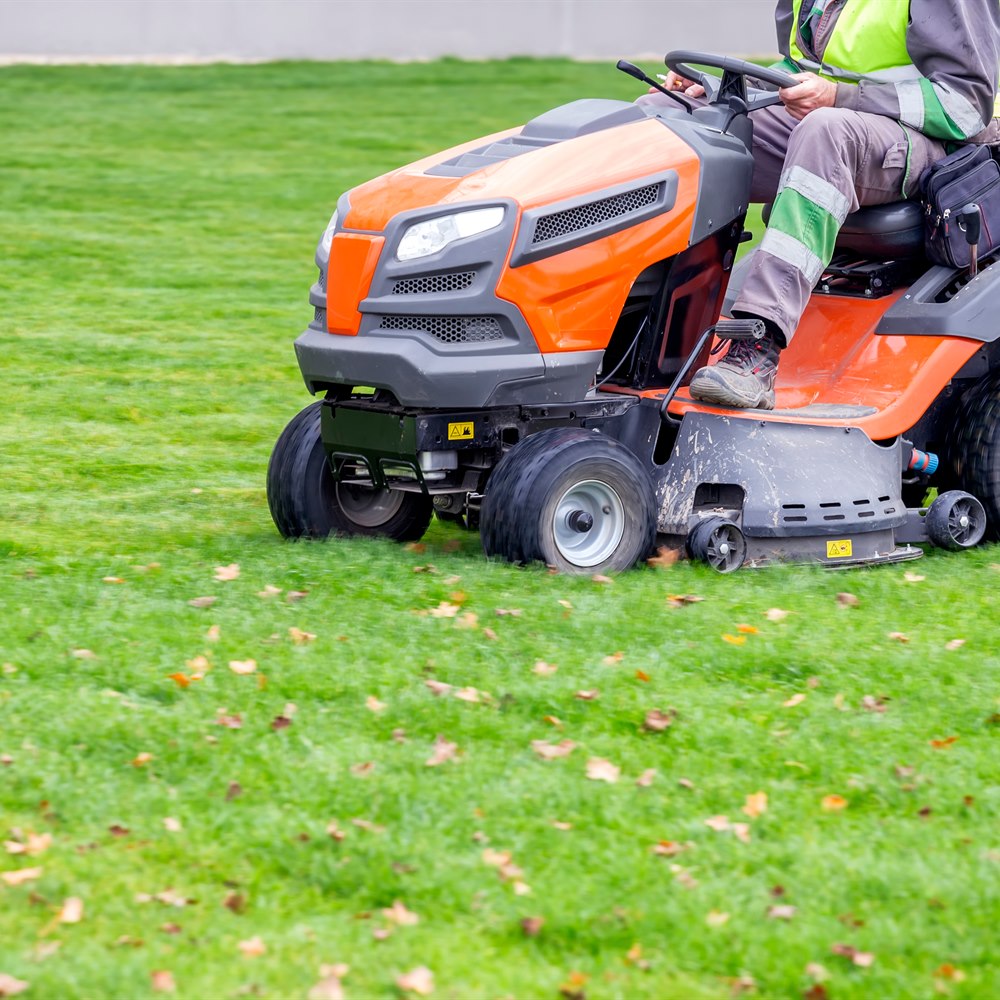 Man riding lawn mower in green field