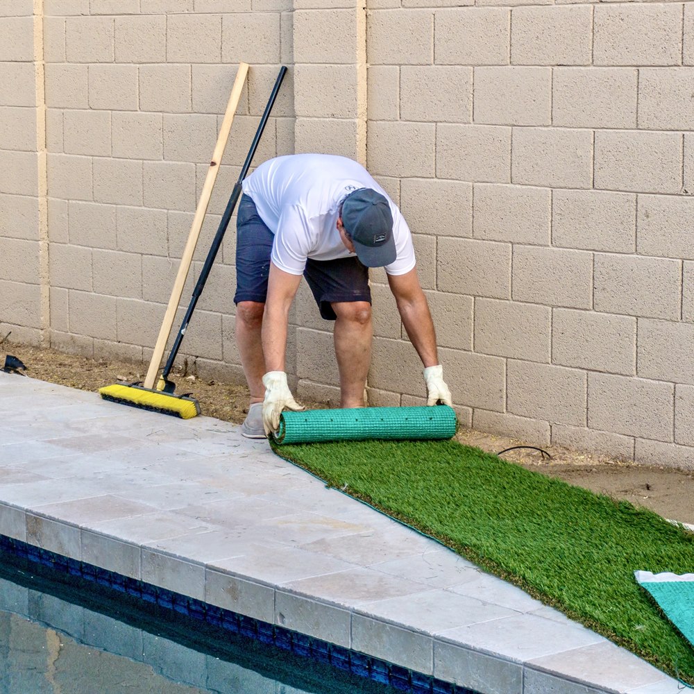 Man unrolling artificial turf near poolside