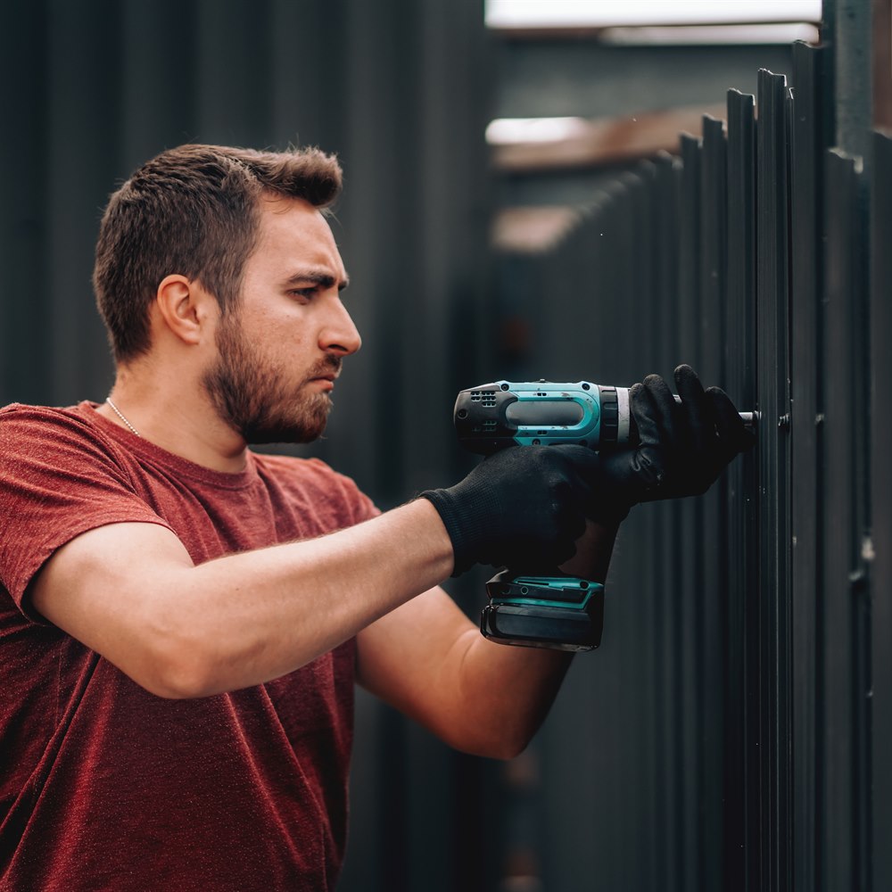 Man using drill on metal fence outdoors
