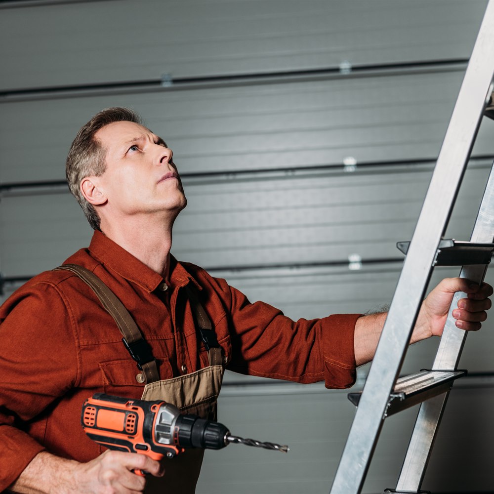 Man with drill on ladder inspecting something