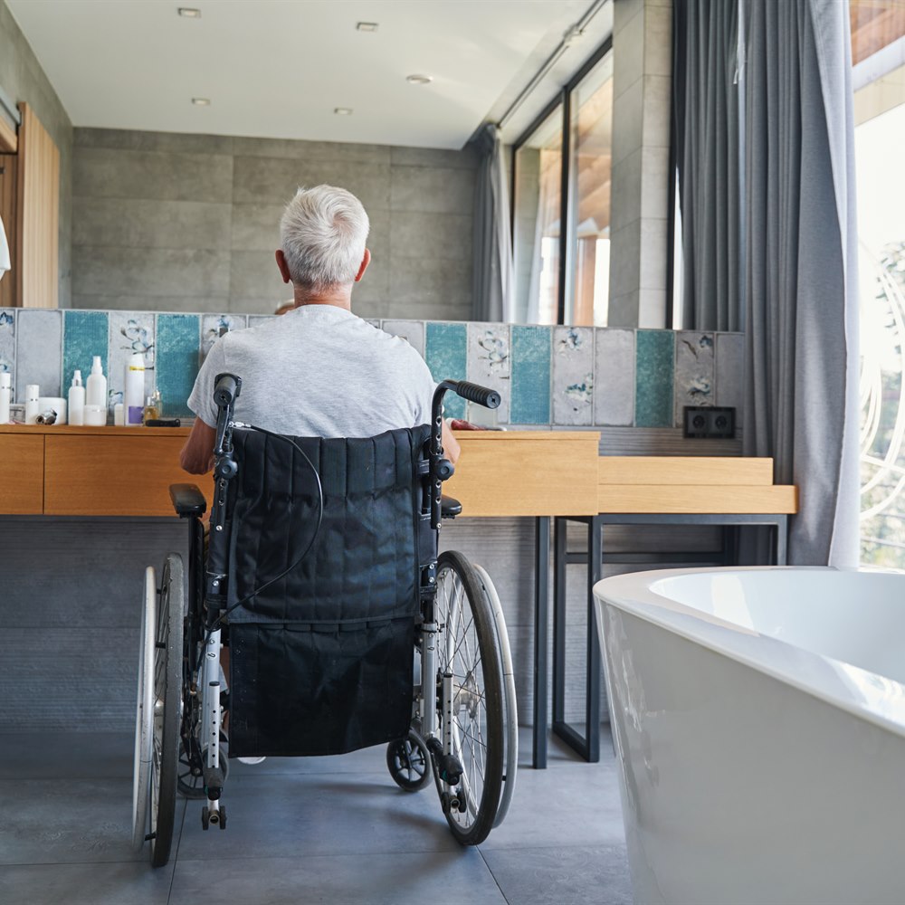 Person in wheelchair using sink in modern bathroom