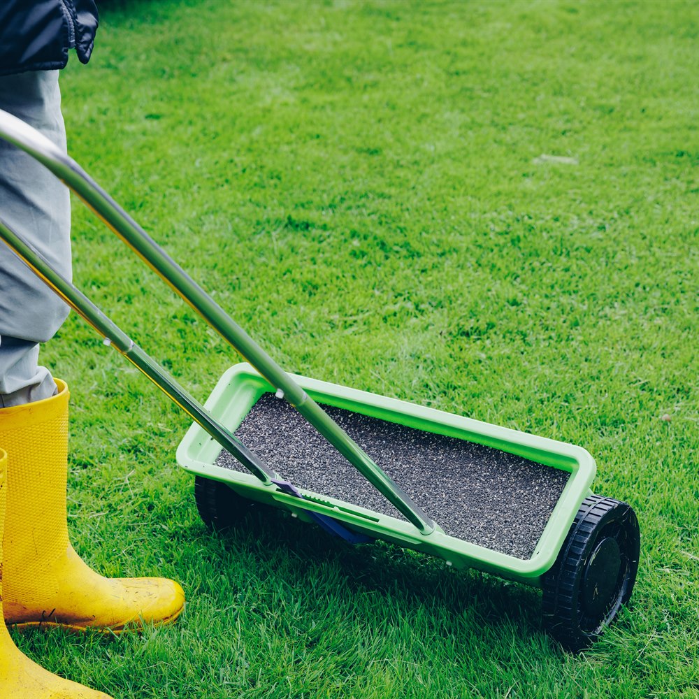 Person in yellow boots using a lawn spreader