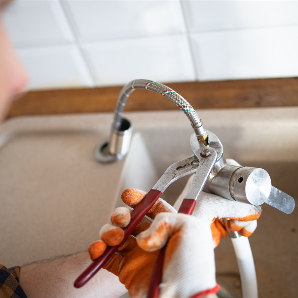 Plumber fixing faucet in a home kitchen sink