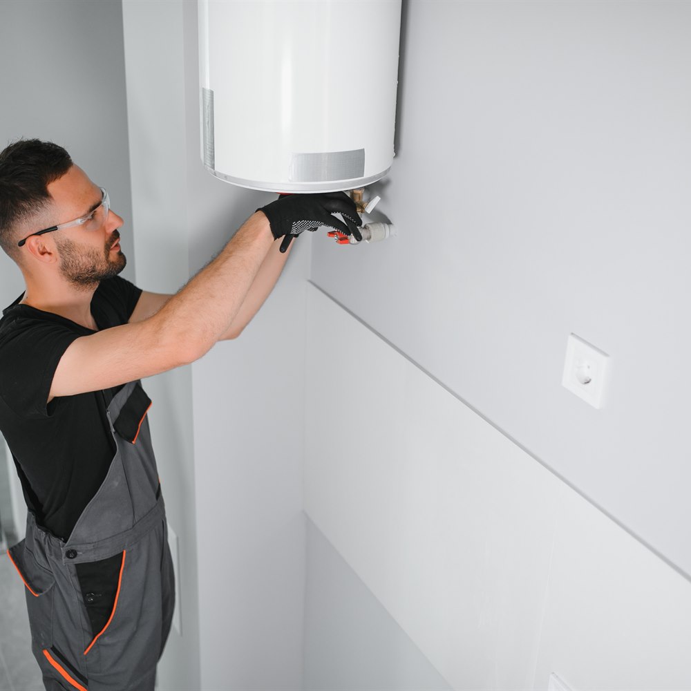 Plumber in overalls fixing a white water heater