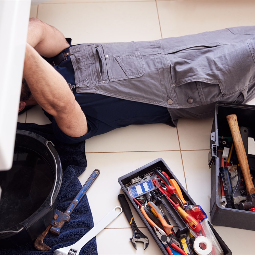 Plumber lying under sink with plumbing tools