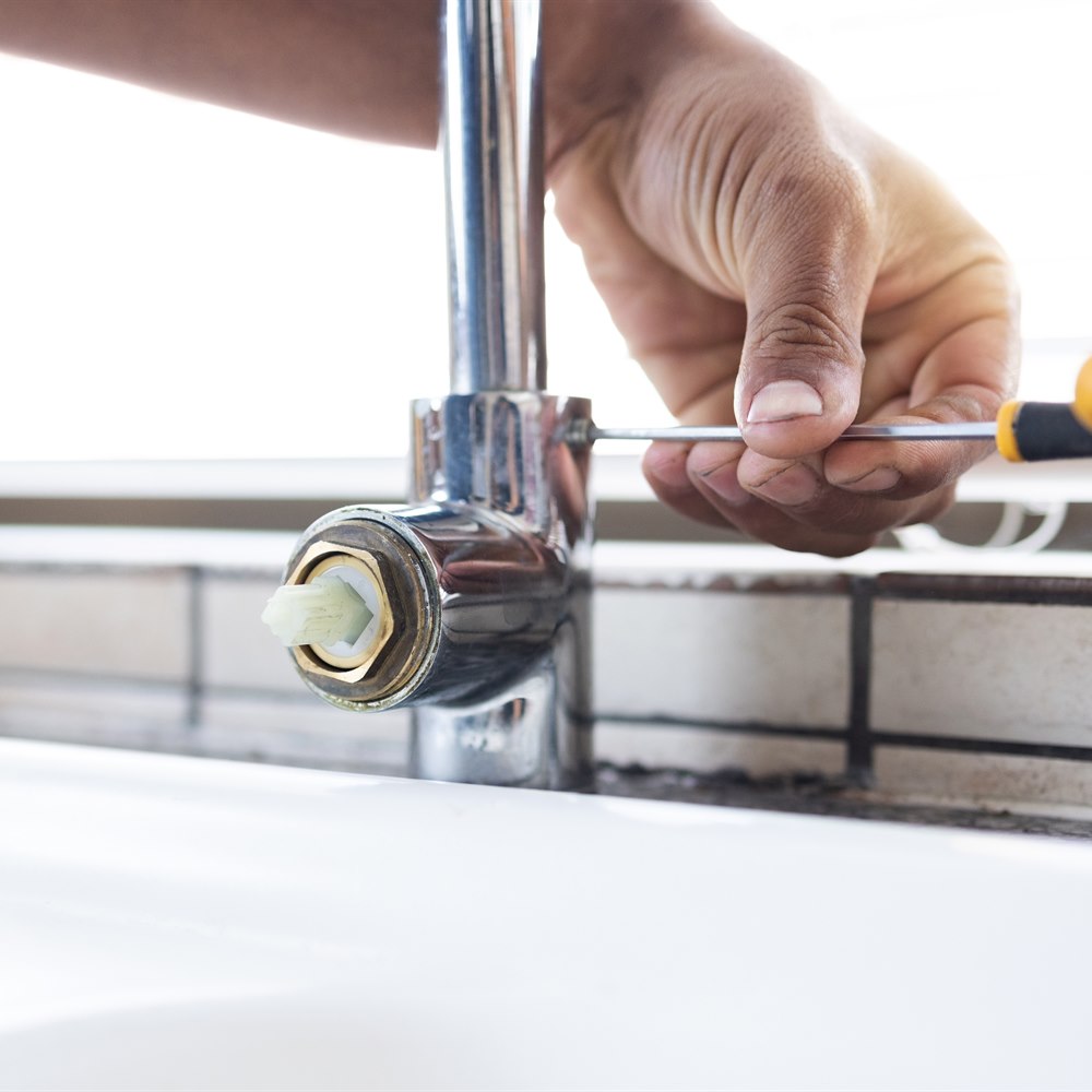 Plumber repairing faucet with screwdriver in sink