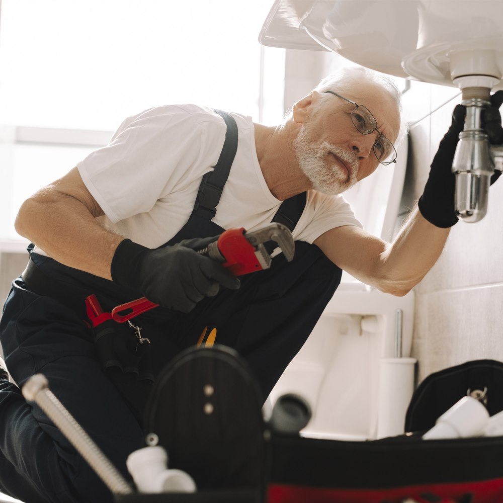 plumber-repairs-sink-in-a-brightly-lit-bathroom Plumber repairs sink in a brightly lit bathroom
