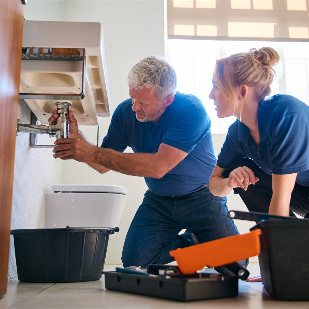 Plumbers repairing sink plumbing in bright bathroom