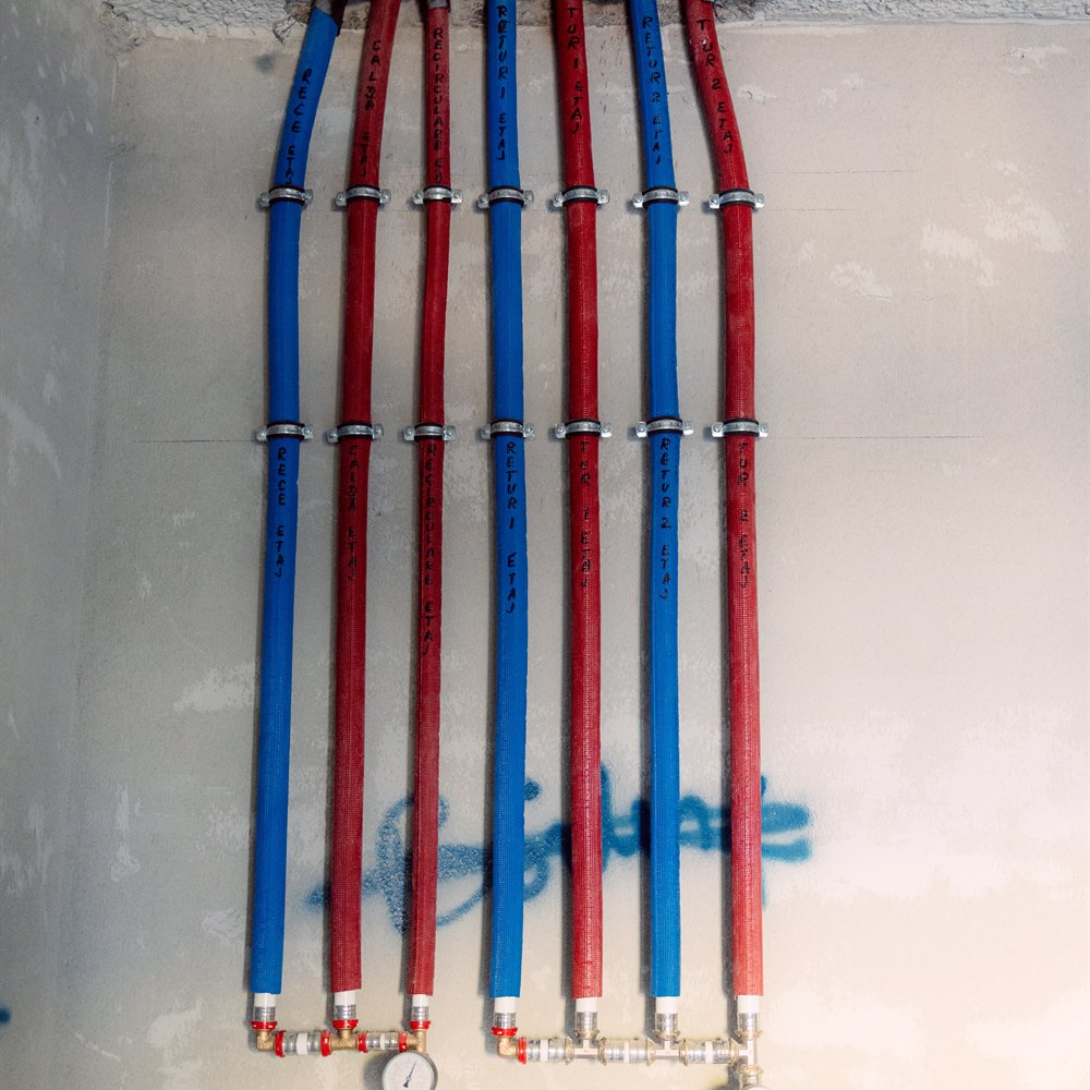 Red and blue pipes attached to gray wall