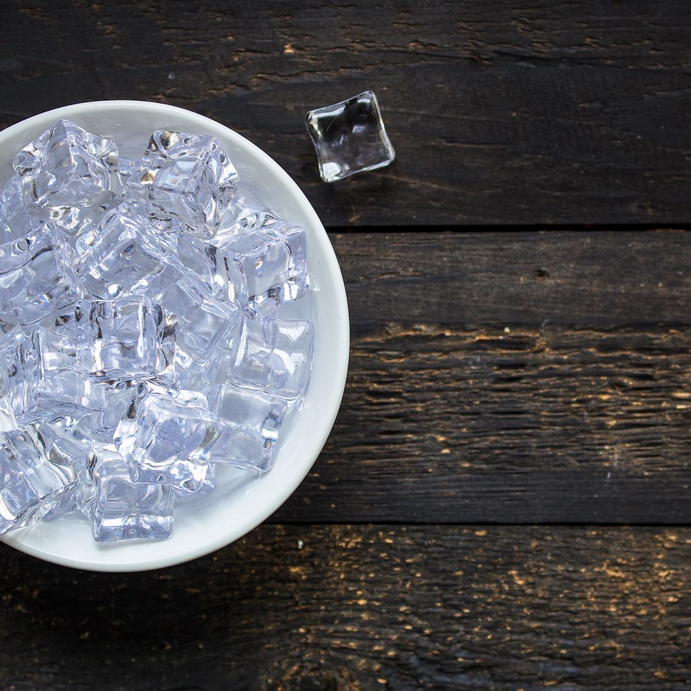 Refreshing ice cubes in white bowl on wood