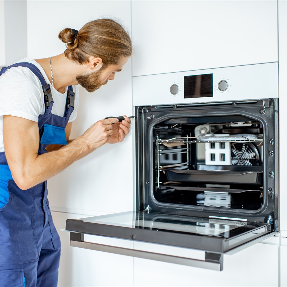 Repairman fixing oven in modern white kitchen