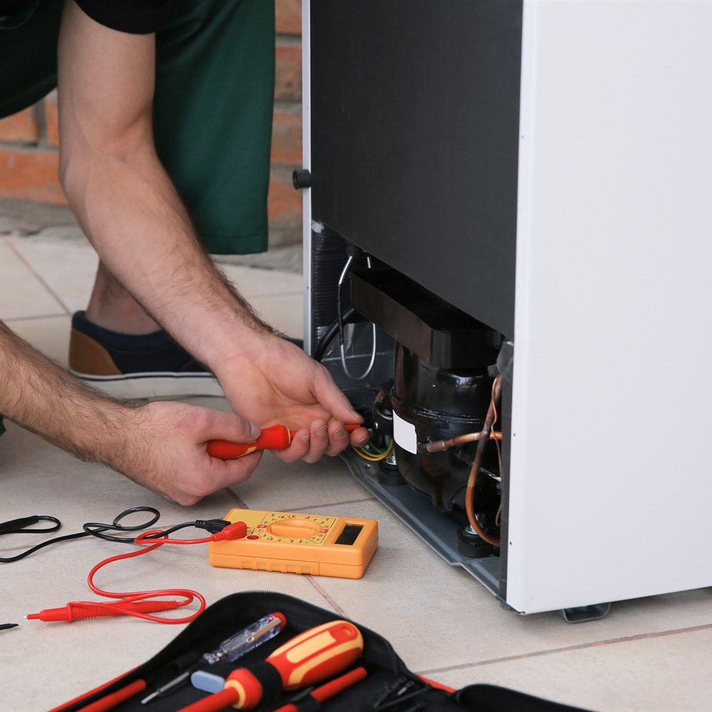Repairman fixing refrigerator with tester in home