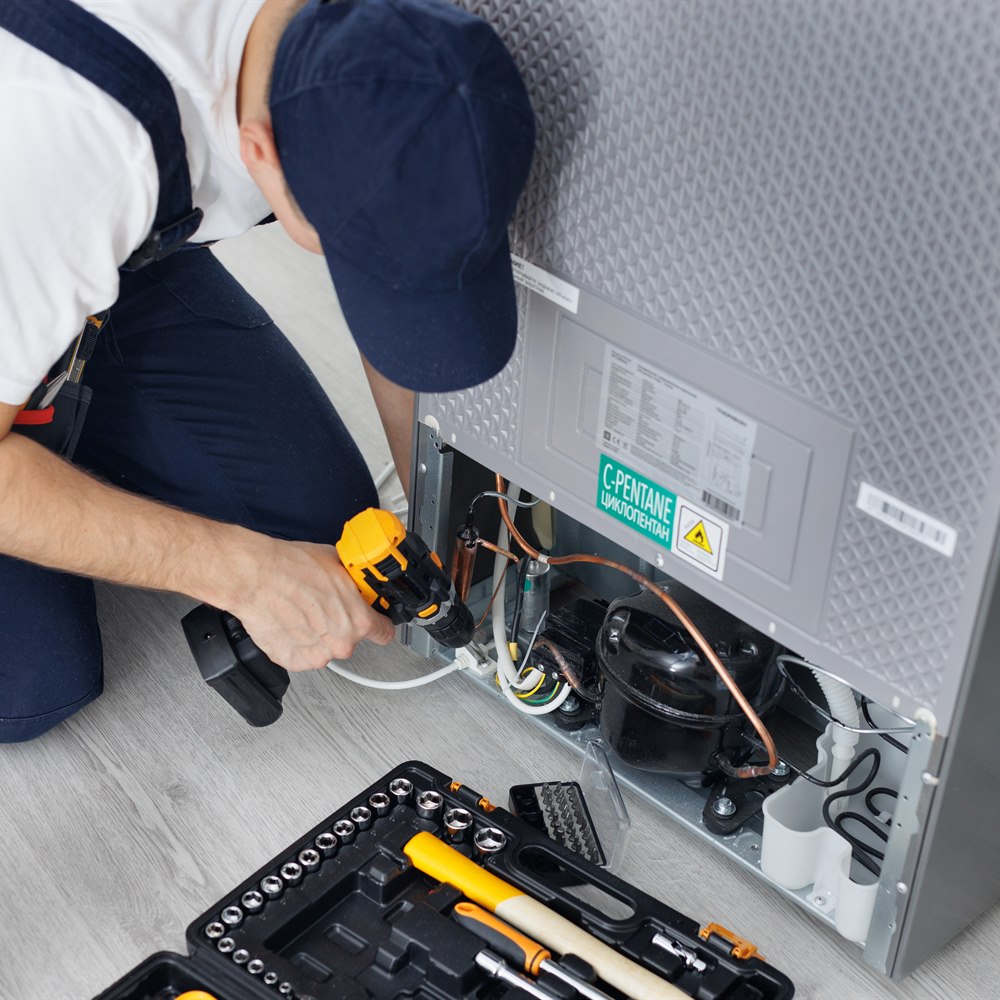 Repairman fixing refrigerator with toolbox in kitchen
