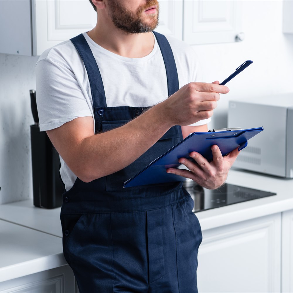 Repairman holding clipboard and pen in kitchen