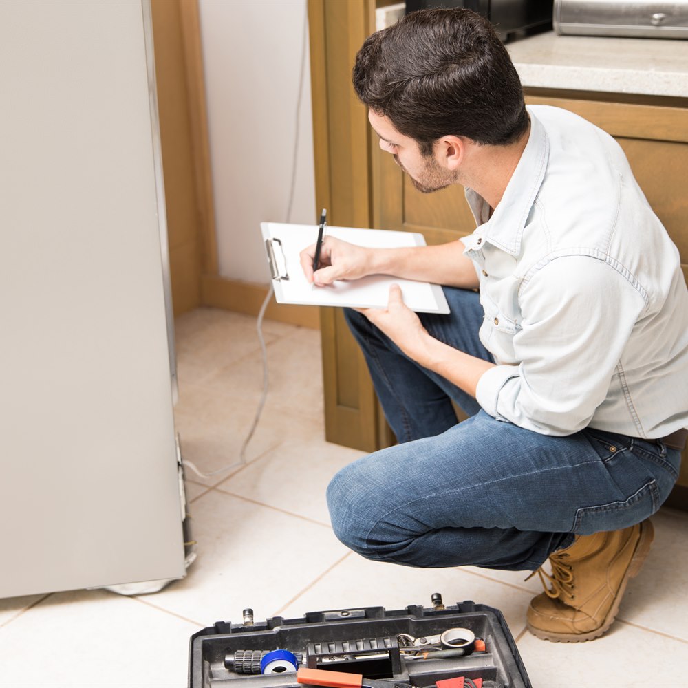 repairman-inspecting-a-refrigerator-and-taking-not Repairman inspecting a refrigerator and taking