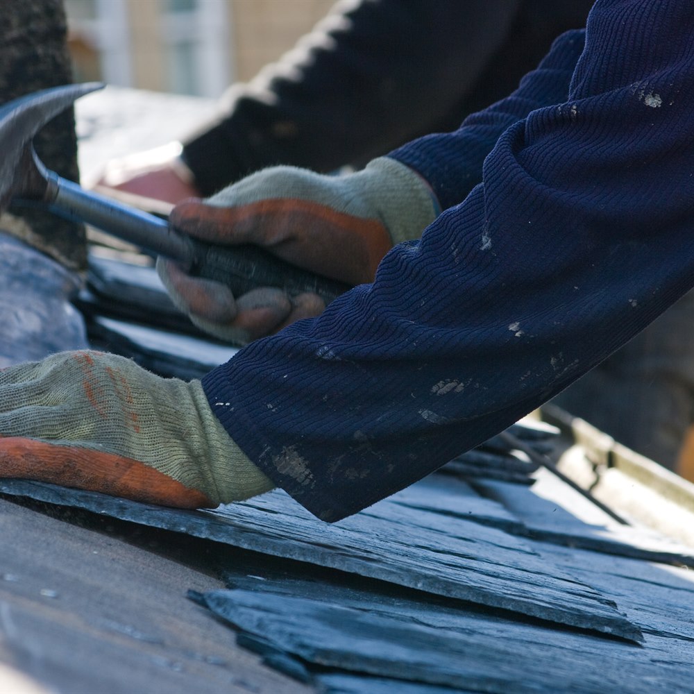 Roofer hammering slate roof tiles