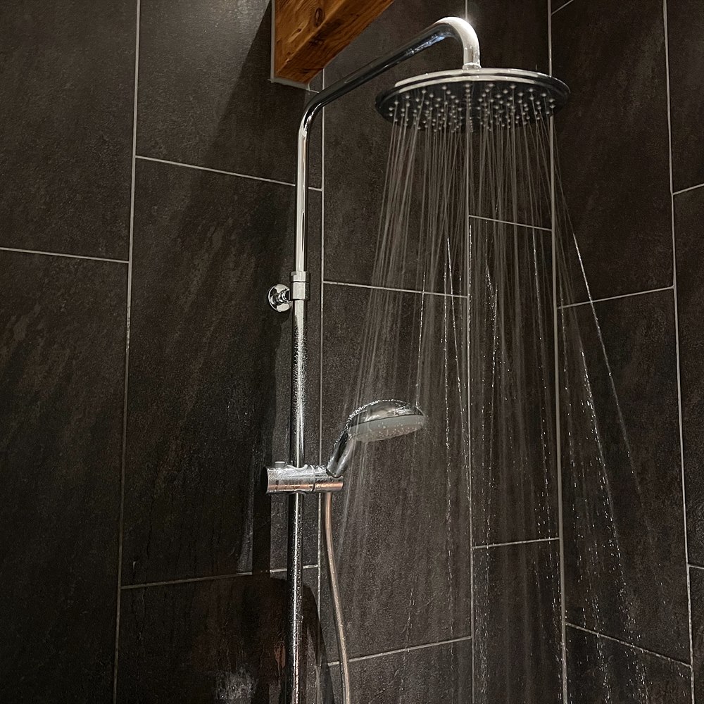 Running shower head with dark grey tiled walls