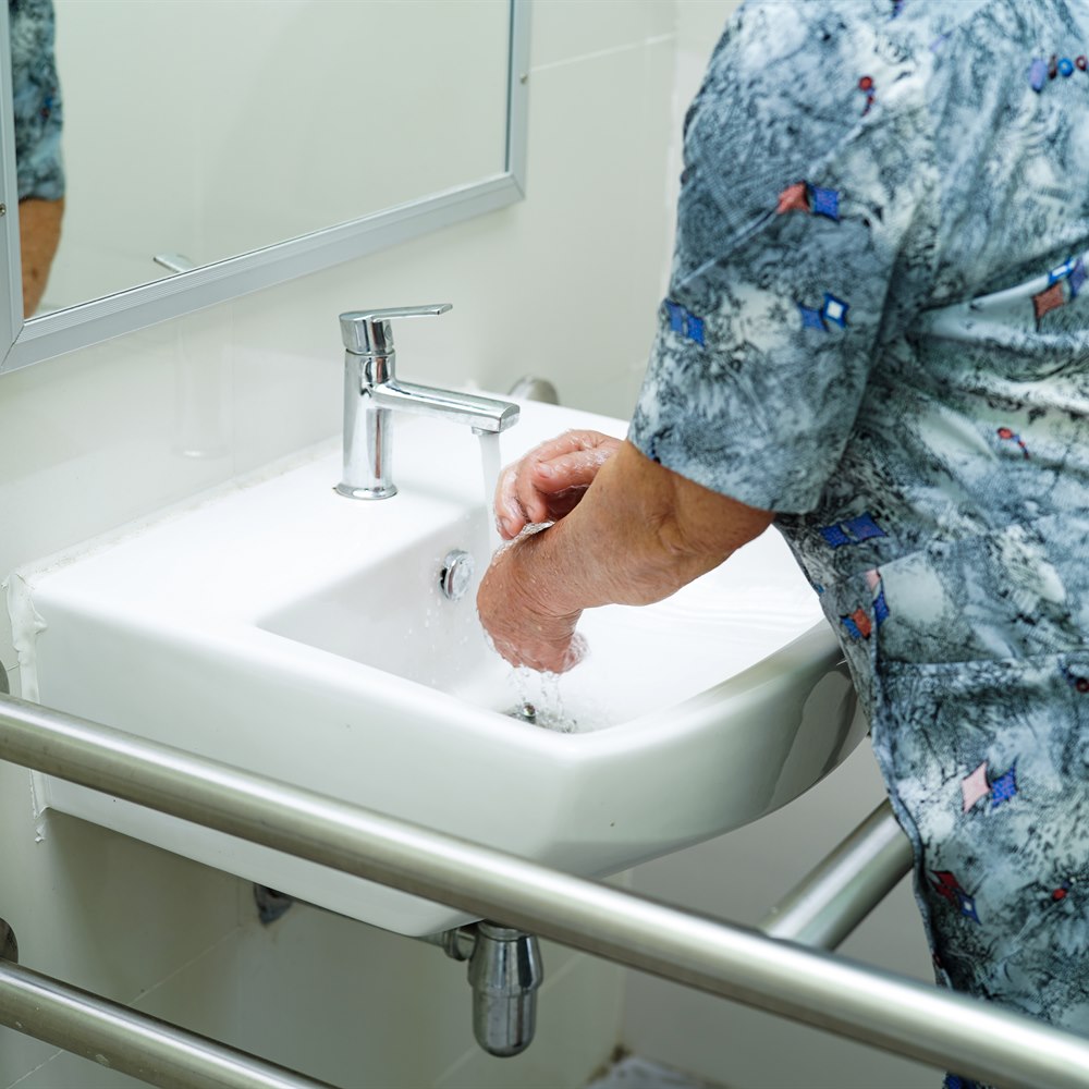 Senior woman washing hands in bathroom sink