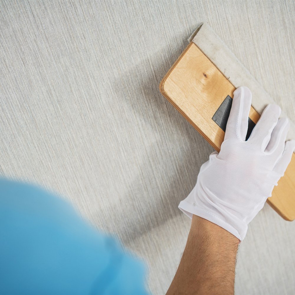 worker-applies-wallpaper-to-wall-with-smoothing Worker applies wallpaper to wall with smoothing