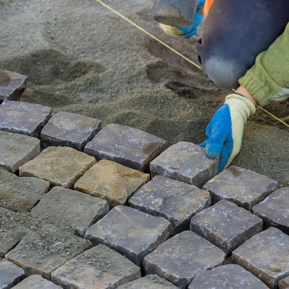 Worker installing cobblestones for a roadway project