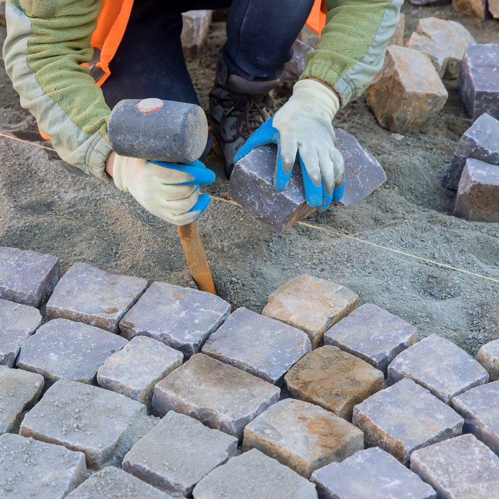 Worker laying stone blocks in street construction
